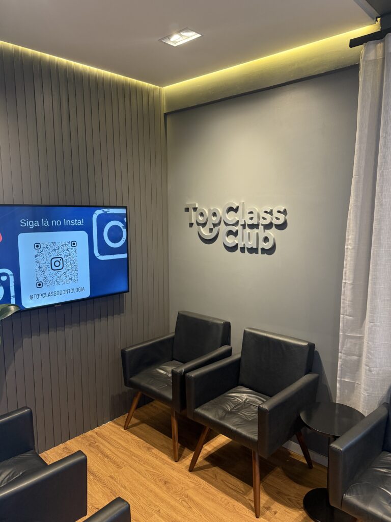 Recepção real da Top Class Odontologia, com poltronas, televisão e painel Top Class Club